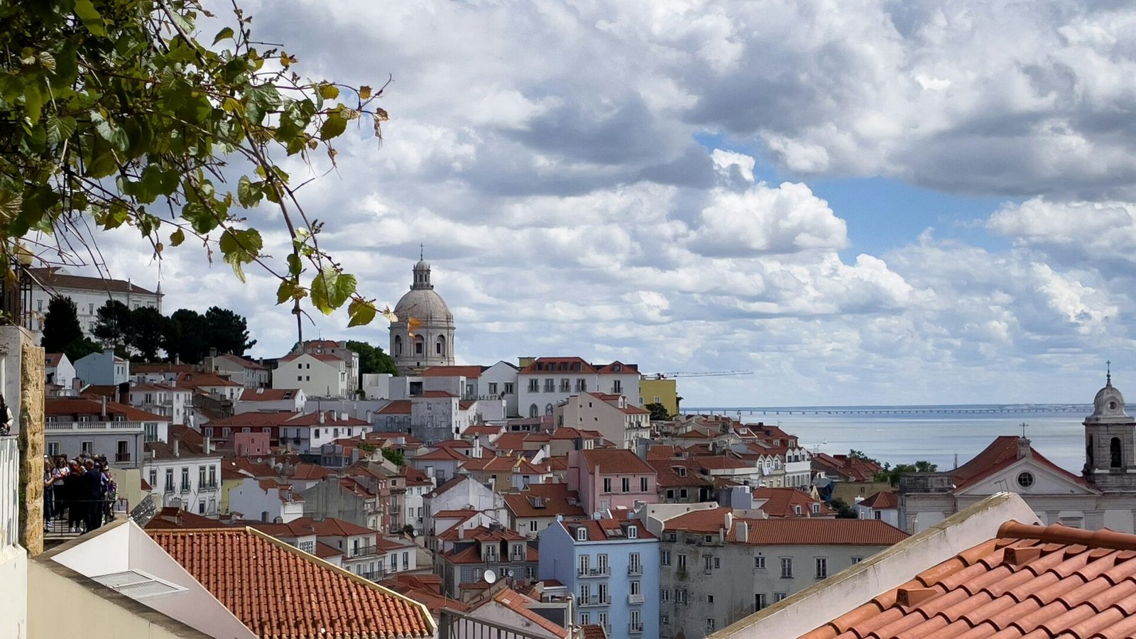 Tejados rojos y una cúpula sobre Alfama, con el río Tajo al fondo.